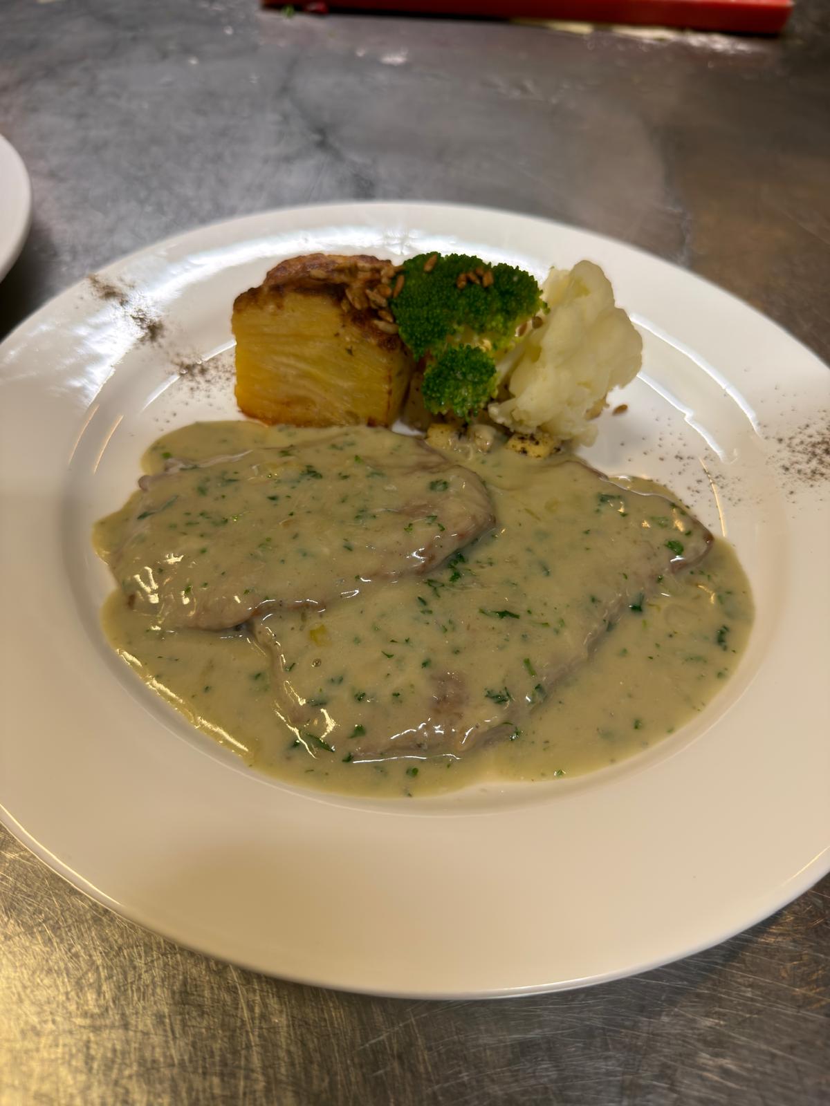 En hvid tallerken med sauce og grøntsager på en metalflade